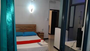 A bedroom with a wooden headboard, a bed with white bedding and a red runner, a ceiling fan, a nightstand with a remote control, and a bathroom visible through an open door.