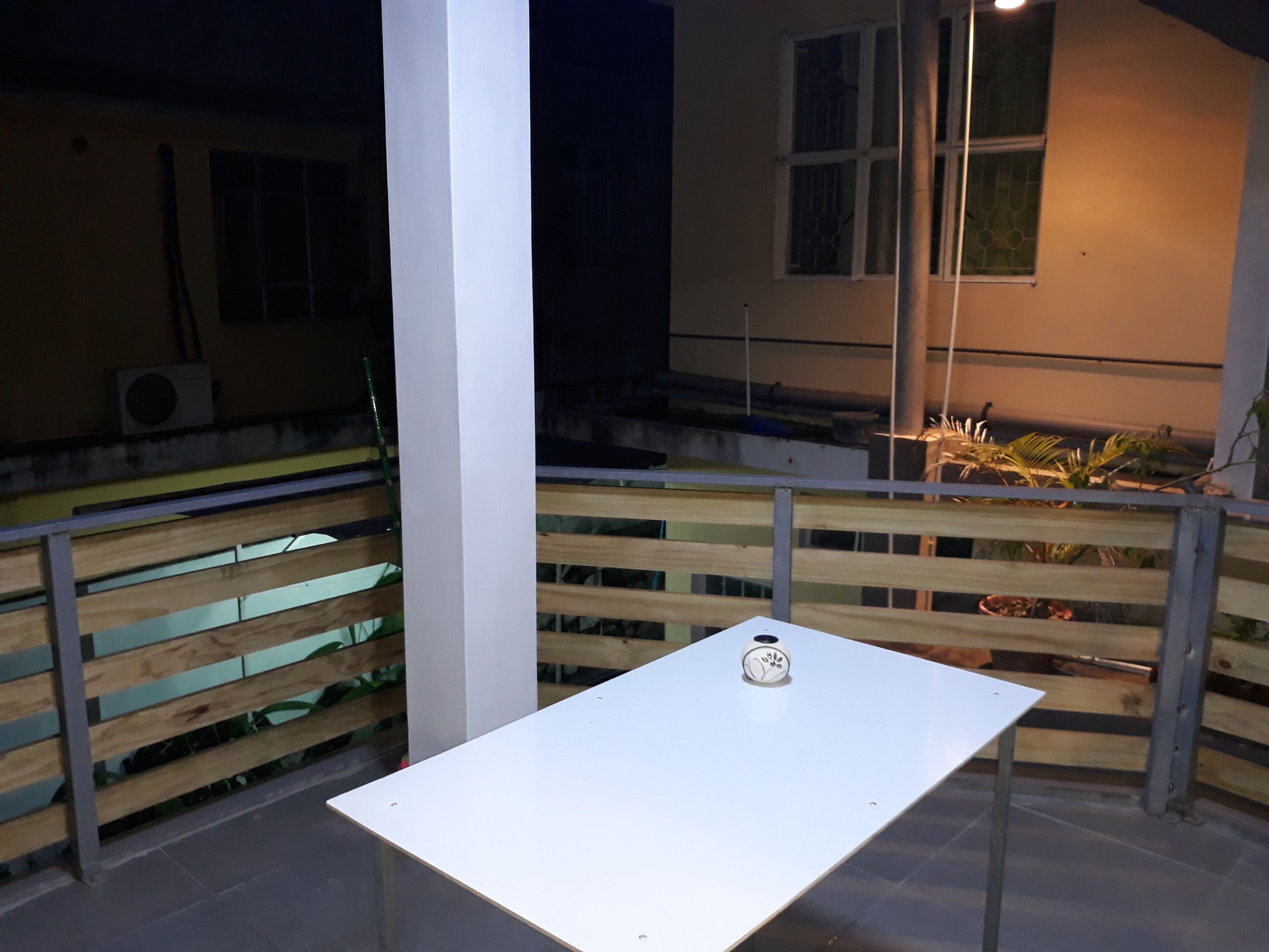 Une table blanche, ornée d’un objet décoratif, est placée devant une rambarde faite de lattes de bois.