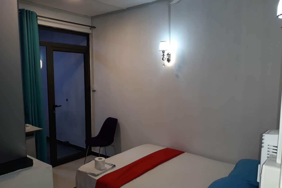 A hotel room with a bed, a chair, a desk, and a door.