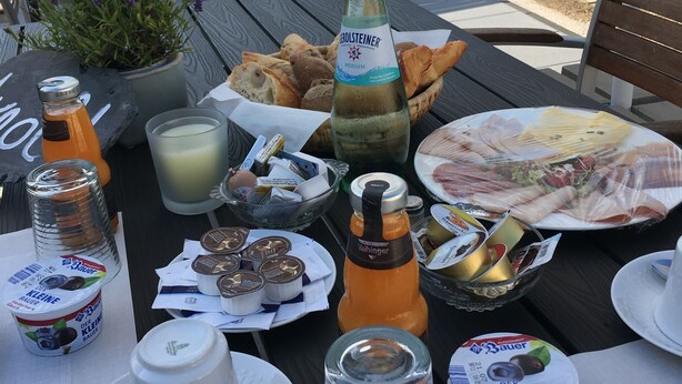 Un espace de restauration en plein air avec une table dressée pour un repas, comprenant du pain, du fromage et des boissons.
