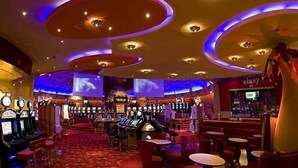 Een casino interieur met gokautomaten, speeltafels en een bar.