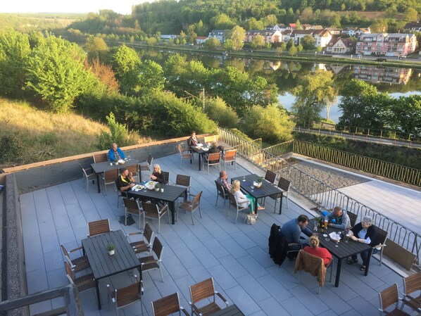 A rooftop terrace with outdoor seating and a view of a river and buildings.
