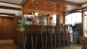 Een bar met houten barstoelen, een bargedeelte en een display met flessen.