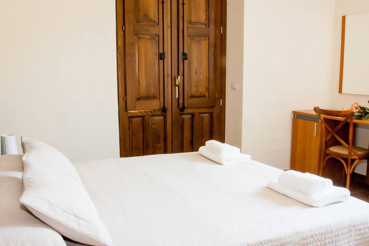 Ein Hotelzimmer mit einem großen Bett, einem Holzschrank, einem Schreibtisch mit Stuhl und einem Spiegel an der Wand.