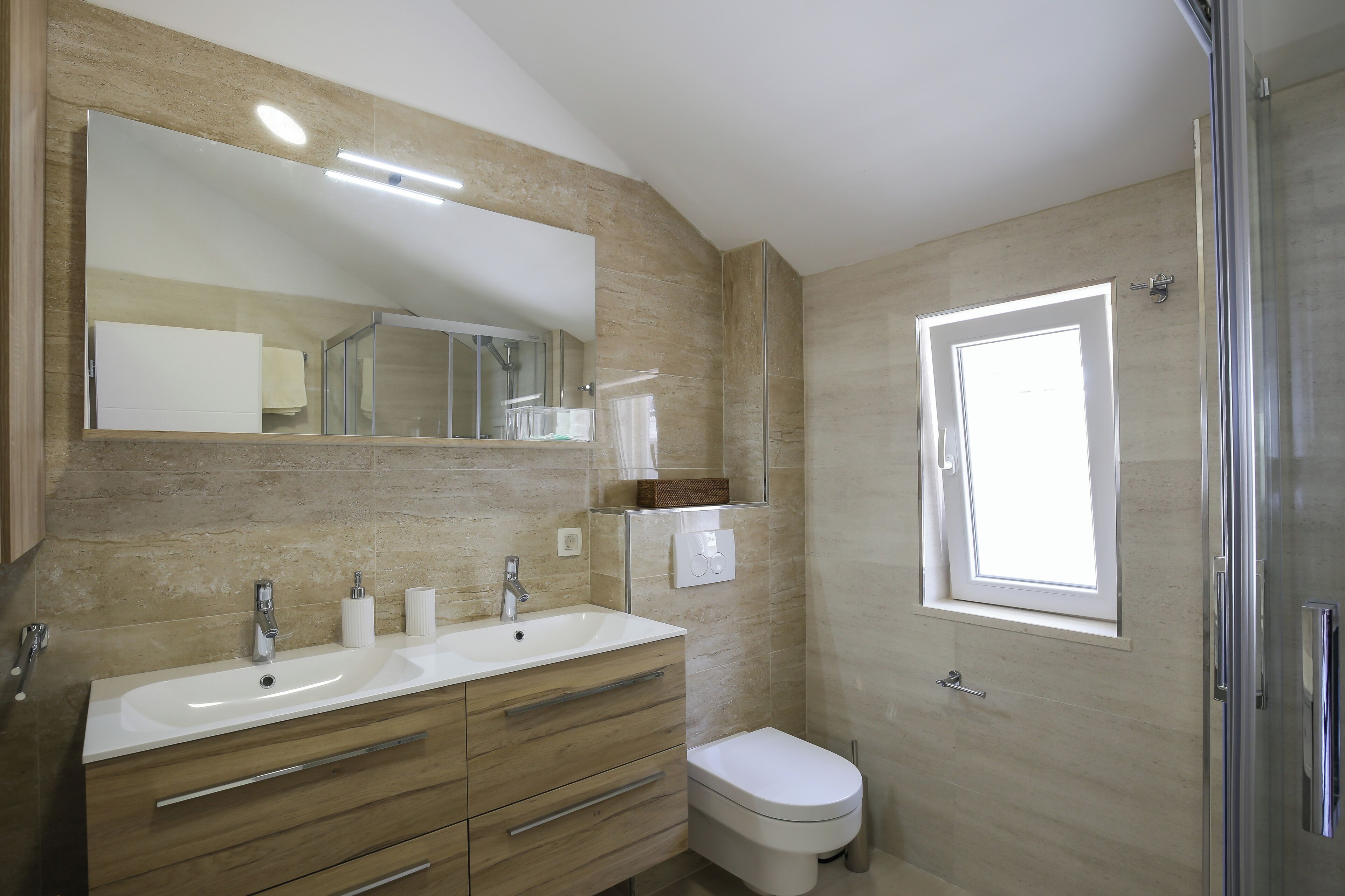 Un bagno moderno con uno specchio grande, due lavandini, un water e una doccia.