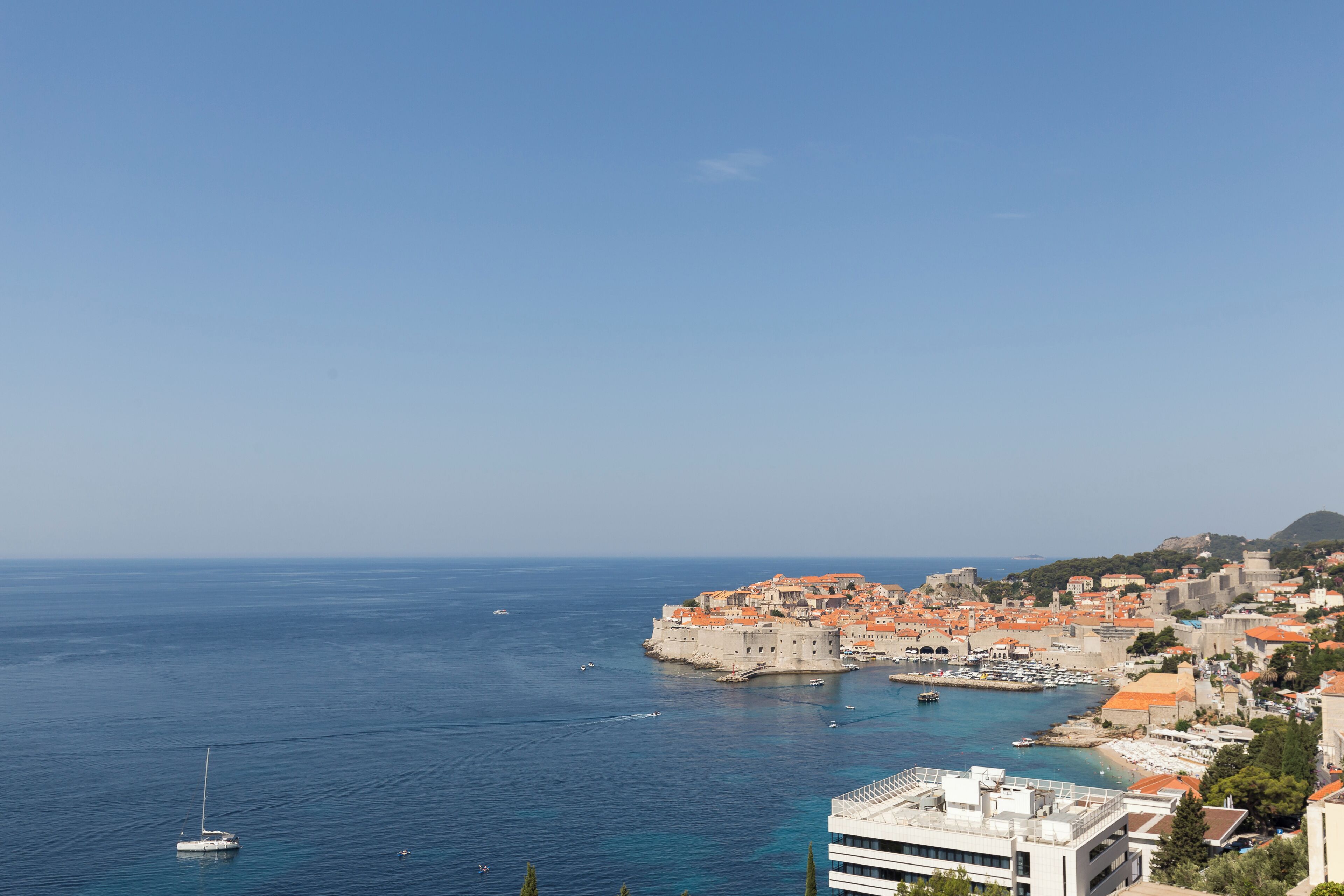 A coastal town with historic buildings, a marina, and a clear blue sky.
