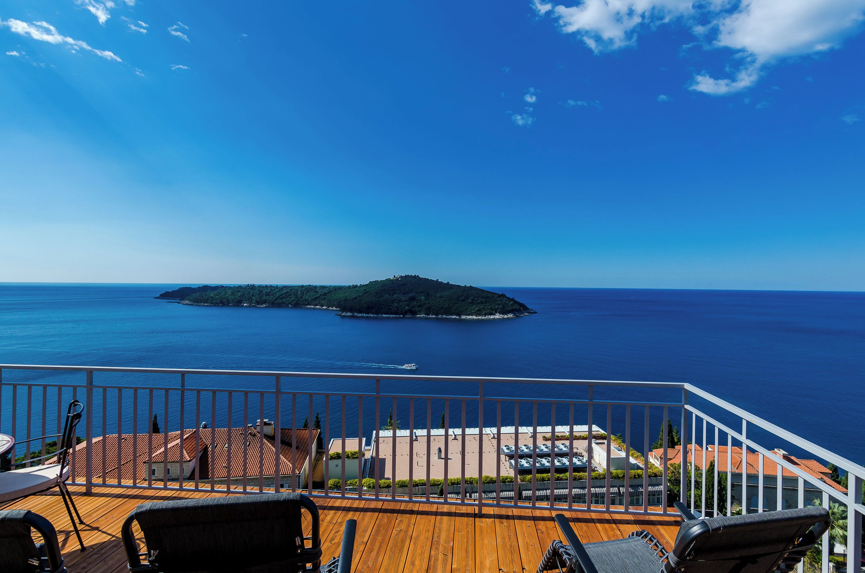 Eine Holzterrasse mit Sitzgelegenheiten im Freien, mit Blick auf ein Gewässer und eine kleine Insel.