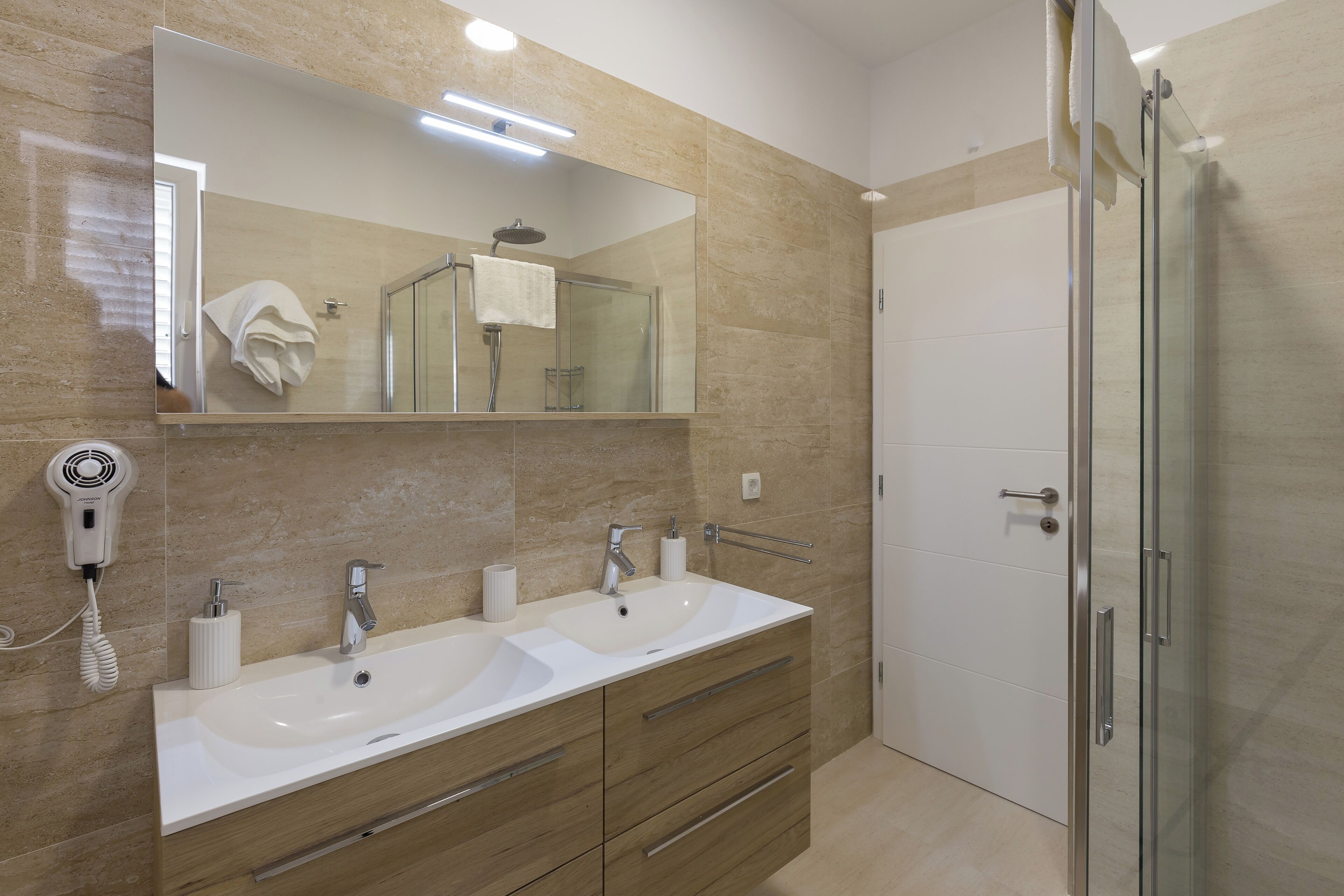 A modern bathroom with two sinks, a large mirror, and a glass shower enclosure.