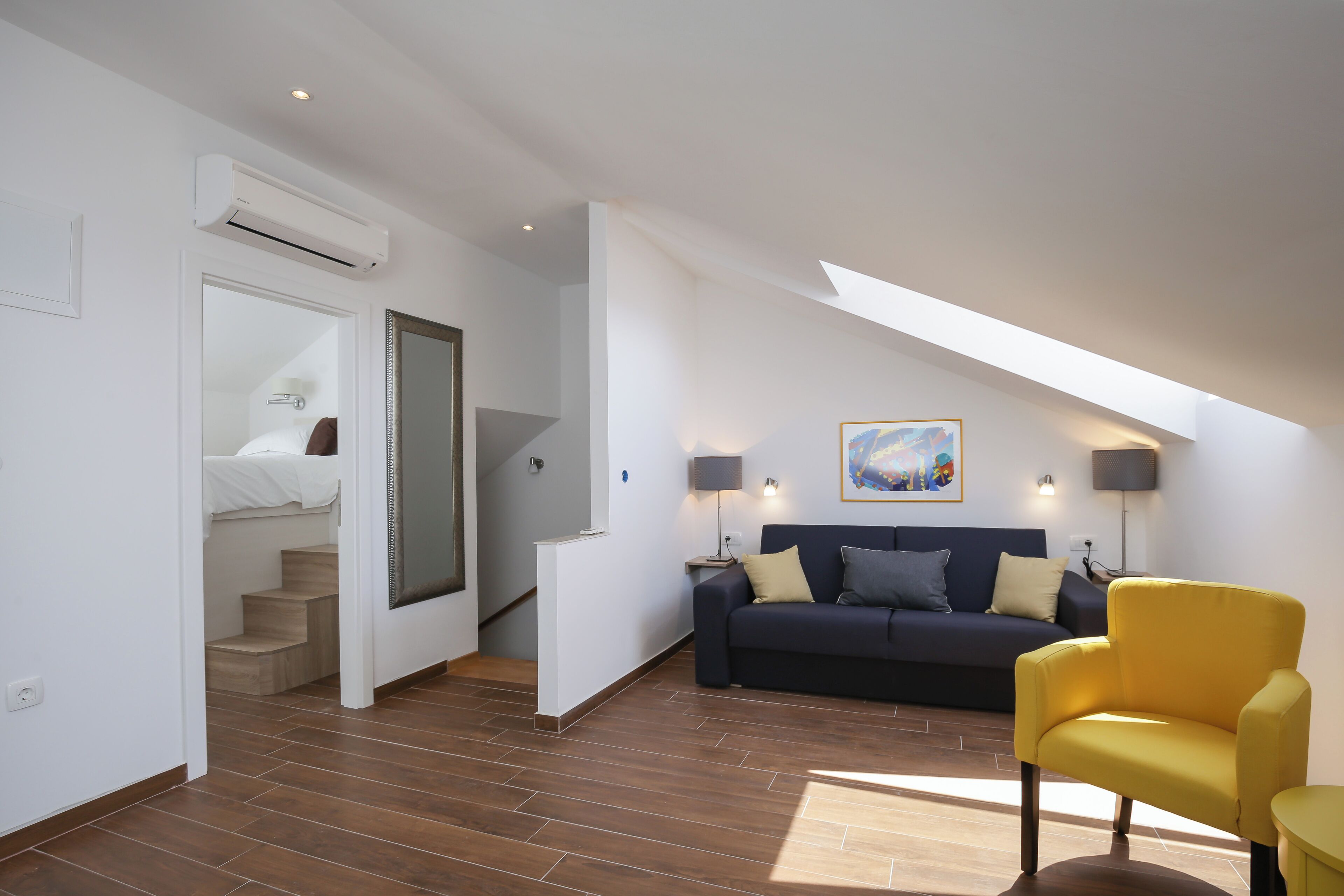 A modern living room with a dark blue sofa, a yellow armchair, and a staircase leading to a bedroom.