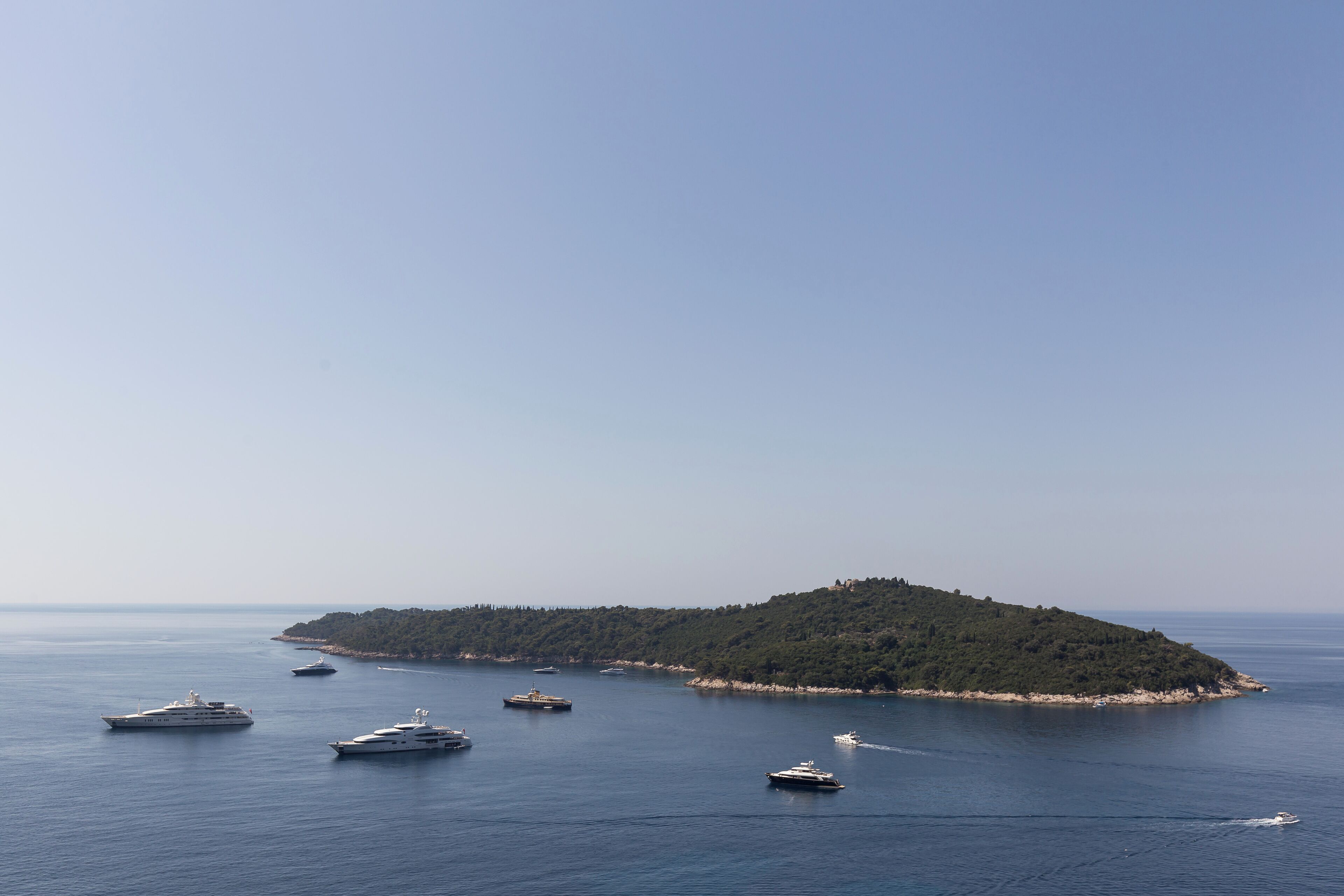 A coastal scene with several yachts anchored near a small island.