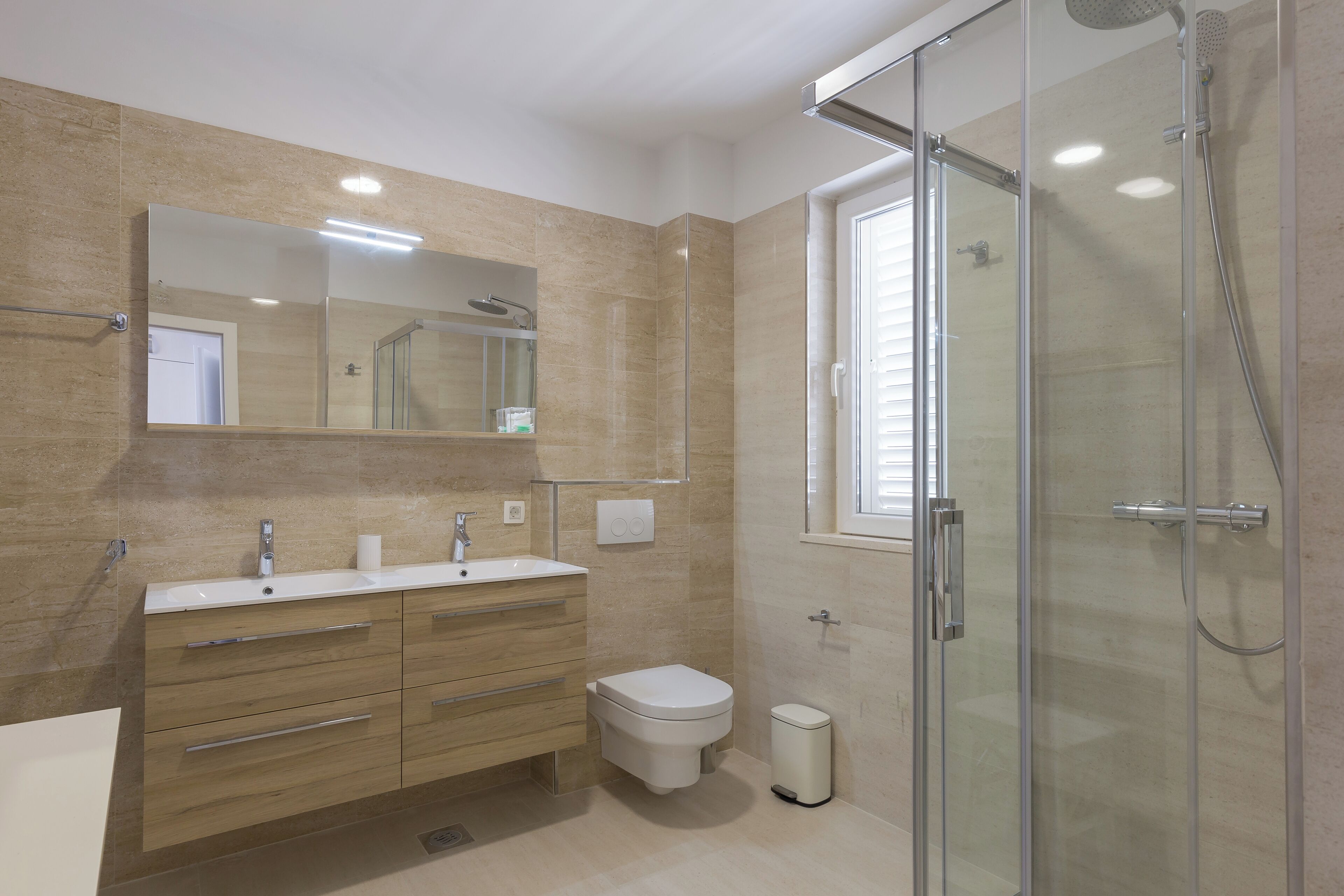Un baño moderno con cabina de ducha de vidrio, un espejo grande y un mueble de tocador de madera con lavabo e inodoro.