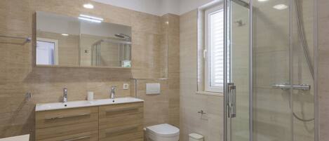 Un baño moderno con cabina de ducha de vidrio, un espejo grande y un mueble de tocador de madera con lavabo e inodoro.