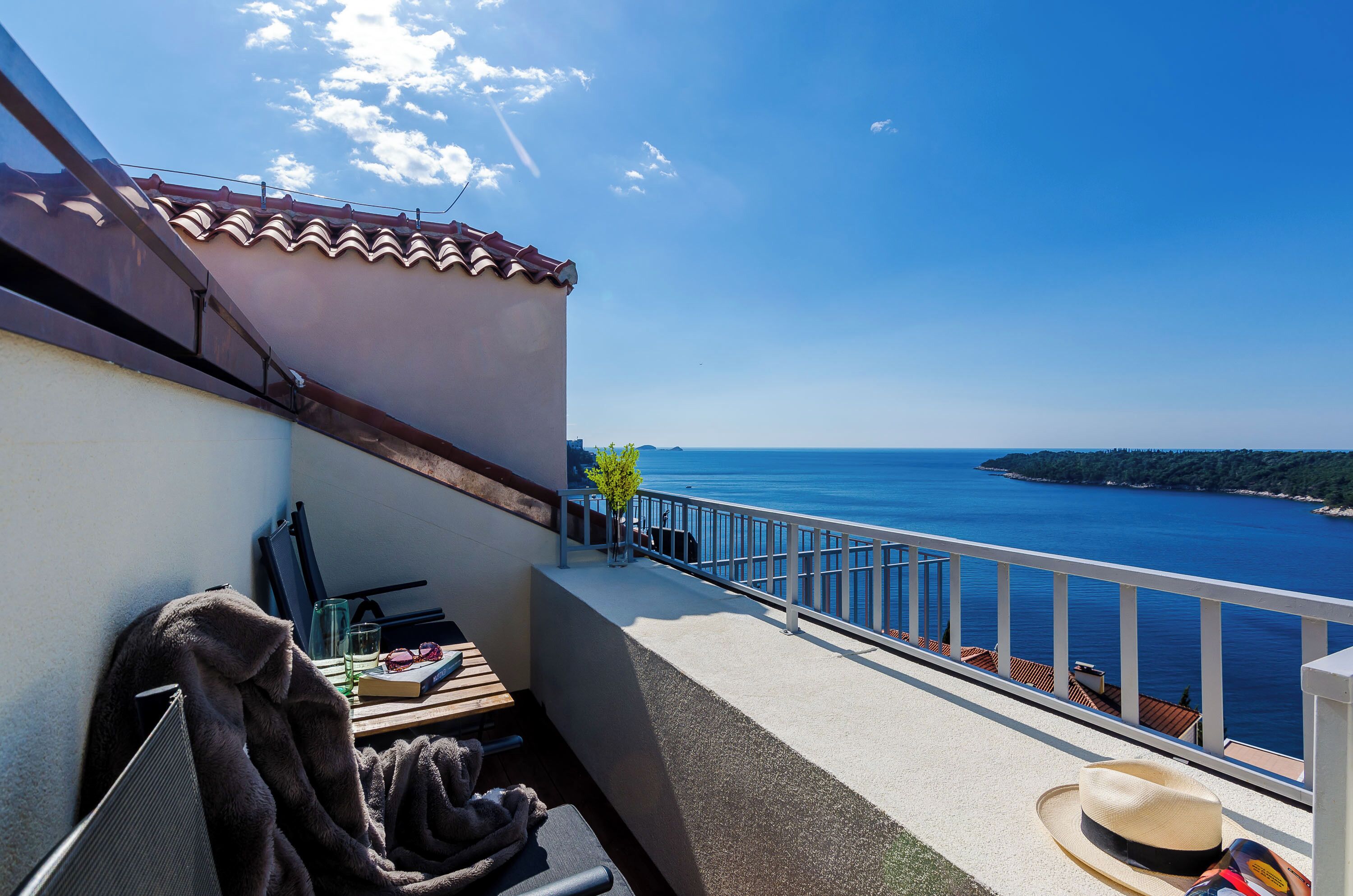 A balcony with a view of the sea, a table with a hat, and a chair.