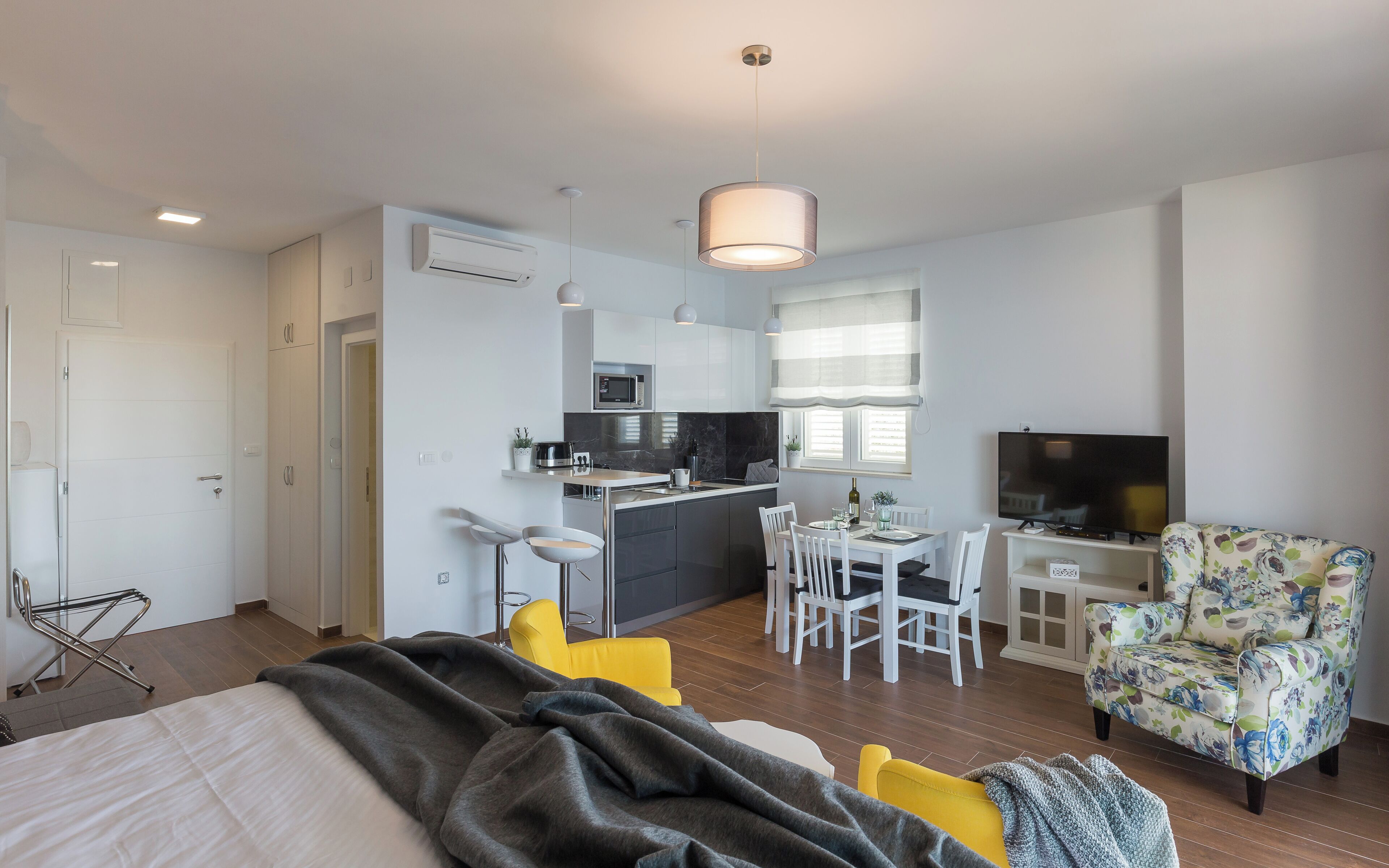 A modern apartment with a kitchen, dining area, and a living room with a TV and floral armchair.