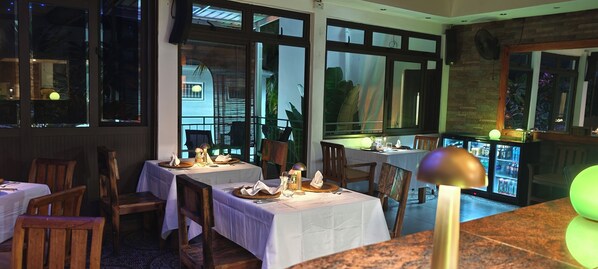 A restaurant with tables set for dining, large windows, and a refrigerator with beverages. - Villa Alizée (Port Louis)
