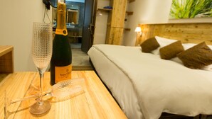 Quarto de hotel com cama, mesa de cabeceira de madeira com uma garrafa de champanhe Veuve Clicquot, um copo e um objeto decorativo.