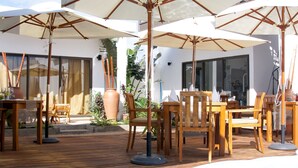A poolside area with wooden furniture and umbrellas, a modern building in the background, and a clear blue sky. - Villa Alizée (Port Louis)