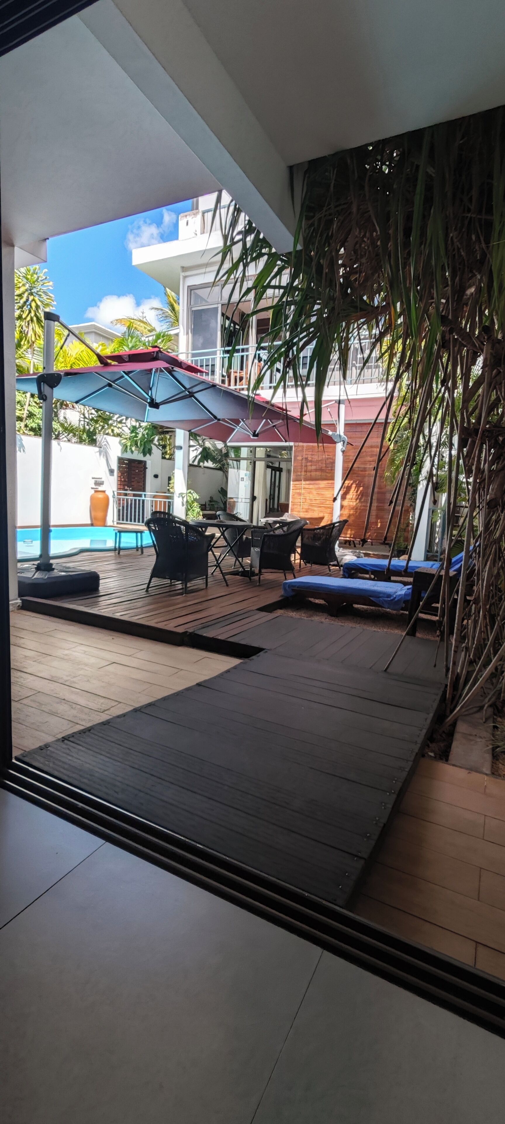 Un espacio al aire libre techado con cubierta de madera, una mesa con sillas y un paraguas azul.