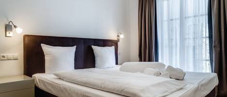 A neatly made bed with white linens, a dark headboard, and two wall-mounted reading lights.