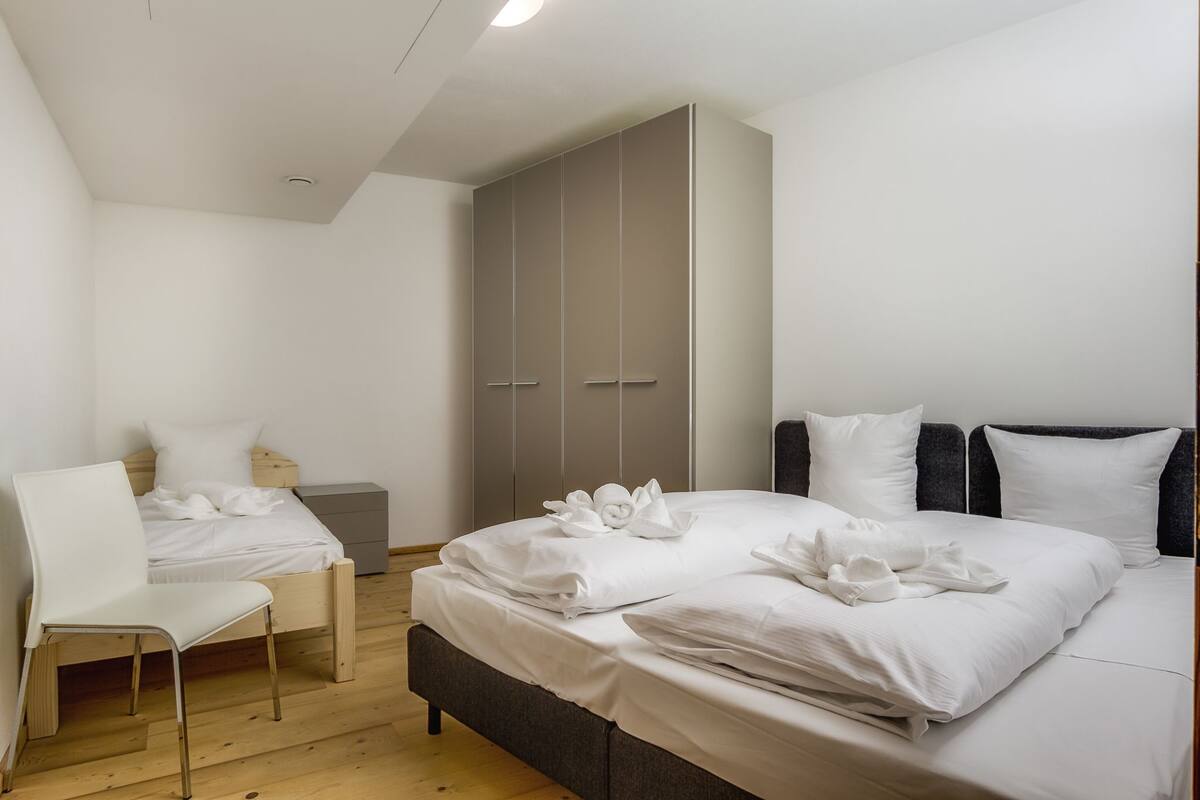 A bedroom with a bed, a chair, a wardrobe, and a bedside table.