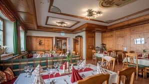 A dining area with wooden paneling, tables set with white tablecloths, and green cushioned benches. - Hotel bayrischer Löwe (Osterhofen)