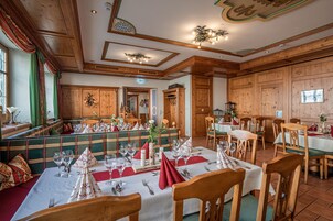 Uma sala de jantar com painéis de madeira, mesas postas com toalhas brancas e bancos acolchoados verdes.