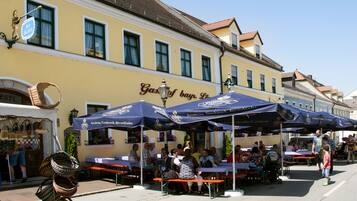 An outdoor café with tables and umbrellas, a yellow building with a sign, and baskets on the sidewalk.
