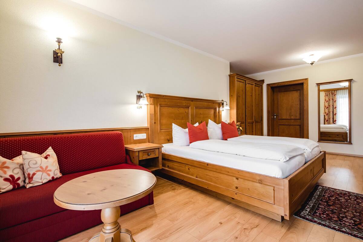 A bedroom with a wooden bed, a red sofa, a small round table, and a wooden wardrobe.