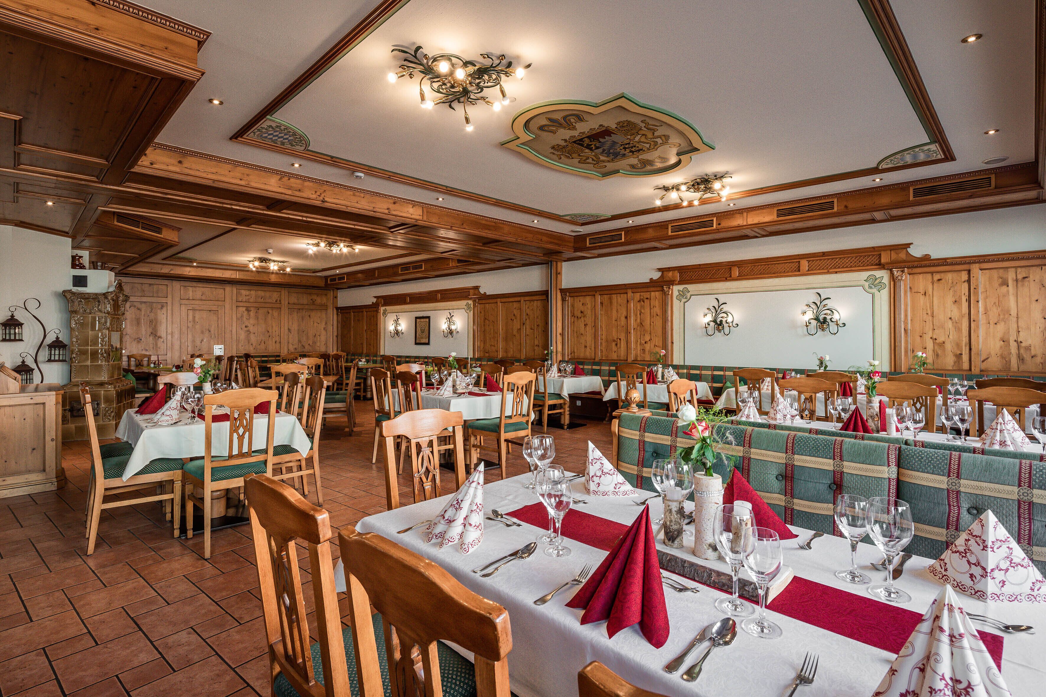 Ein Restaurant mit Holzvertäfelung, mehreren Tischen, die mit weißen Tischdecken und roten Servietten gedeckt sind, und unterschiedlichen Stühlen.