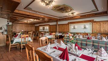 Ein Restaurant mit Holzvertäfelung, mehreren Tischen, die mit weißen Tischdecken und roten Servietten gedeckt sind, und unterschiedlichen Stühlen.