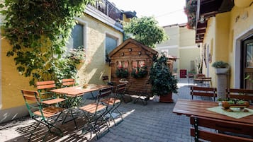 A courtyard with wooden tables and chairs, potted plants, and a small wooden building.