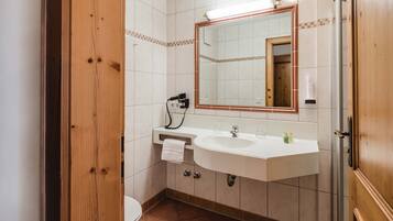 Un baño con puerta de madera, un lavabo blanco, un espejo y una toalla colgada en la pared.