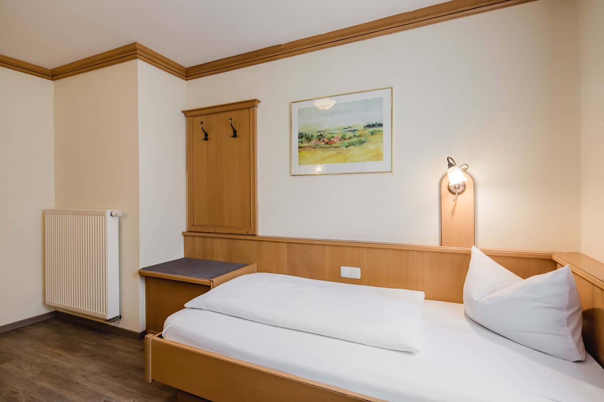 A bedroom with a single bed, a wooden wardrobe, a radiator, and a framed landscape painting on the wall.