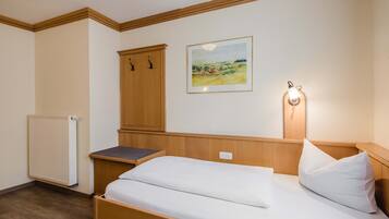 Un dormitorio con una cama individual, un armario de madera, un radiador y un cuadro con un paisaje en la pared.