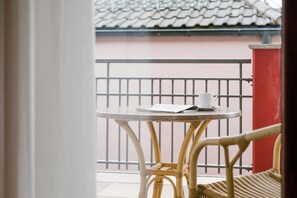 Un balcón con una mesa redonda y una silla de mimbre, con vista a un edificio de tejado a la vista.