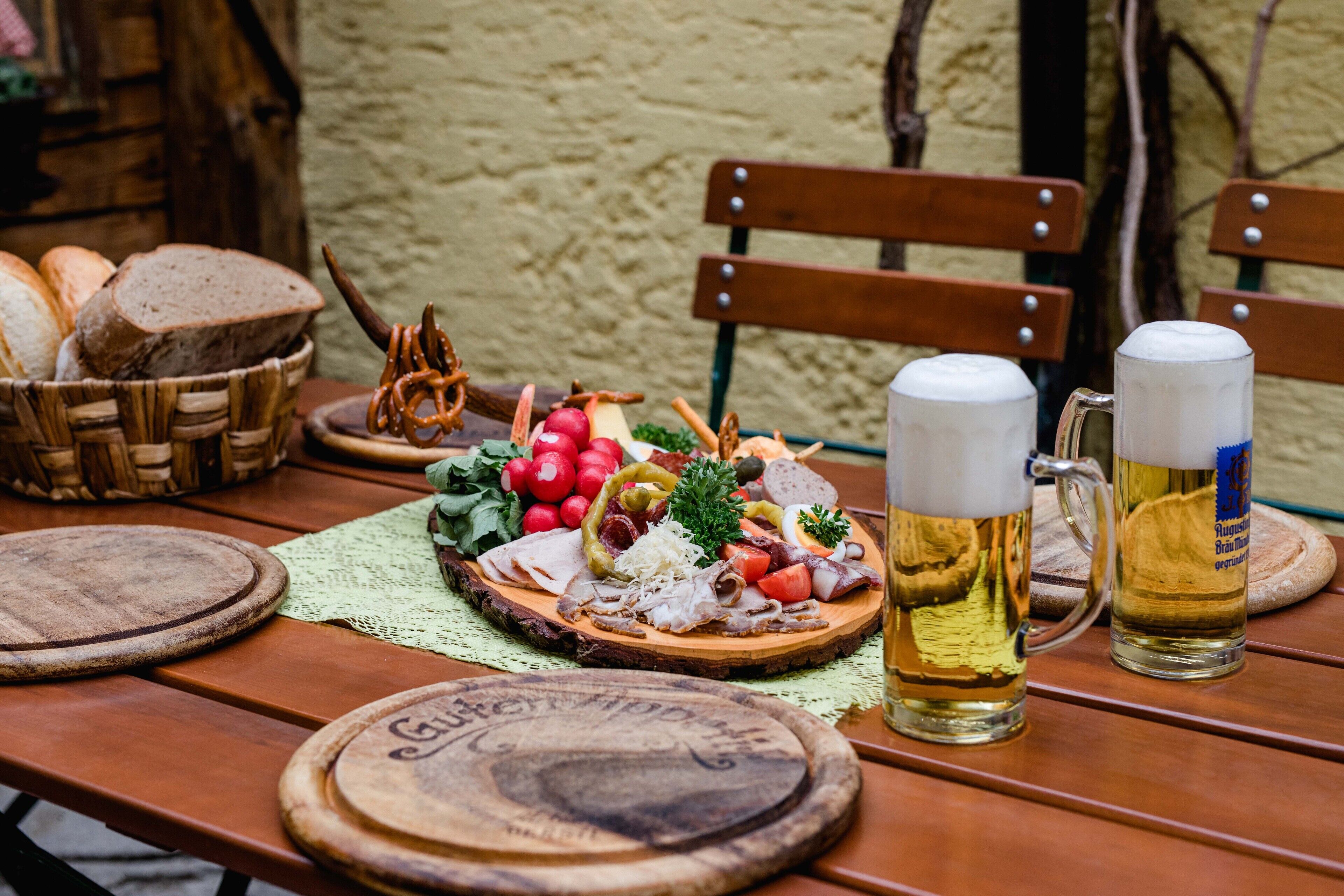 A wooden table with a charcuterie board, two beer mugs, and bread.