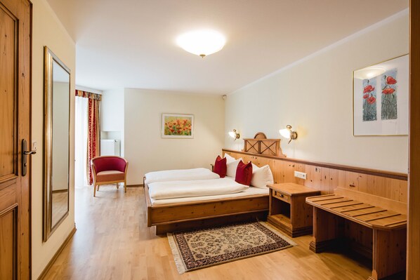 A bedroom with a wooden bed, a chair, a desk, and a mirror.