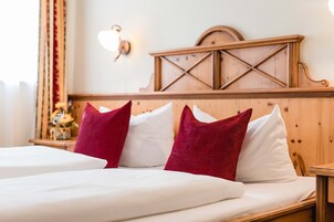 Quarto de hotel com cabeceira de madeira, roupa de cama branca e almofadas vermelhas.