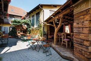 Uma área de café ao ar livre com mesas e cadeiras de madeira, cercada por edifícios com estilo arquitetônico rústico.