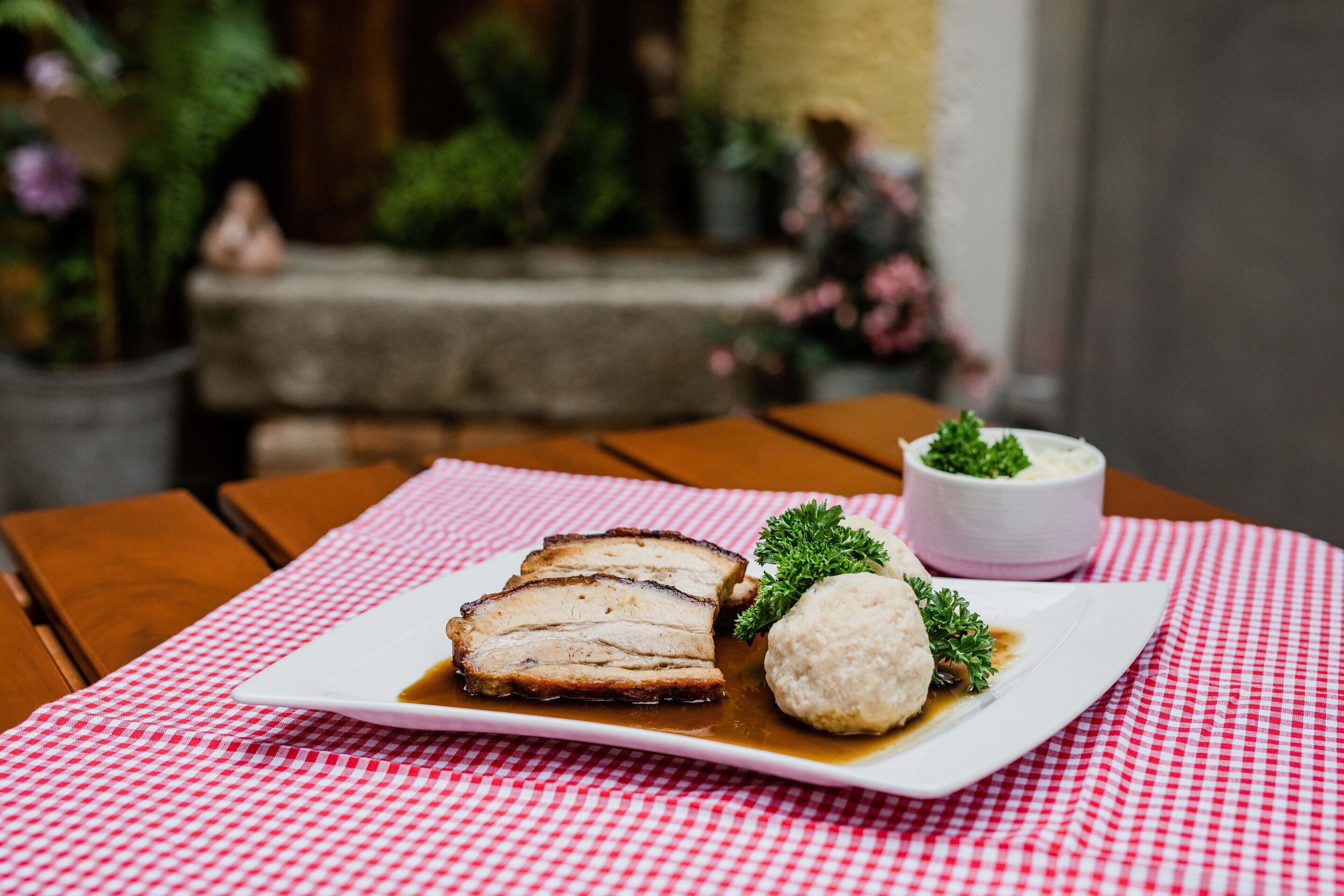 A plate of sliced meat with gravy and dumplings on a checkered tablecloth.