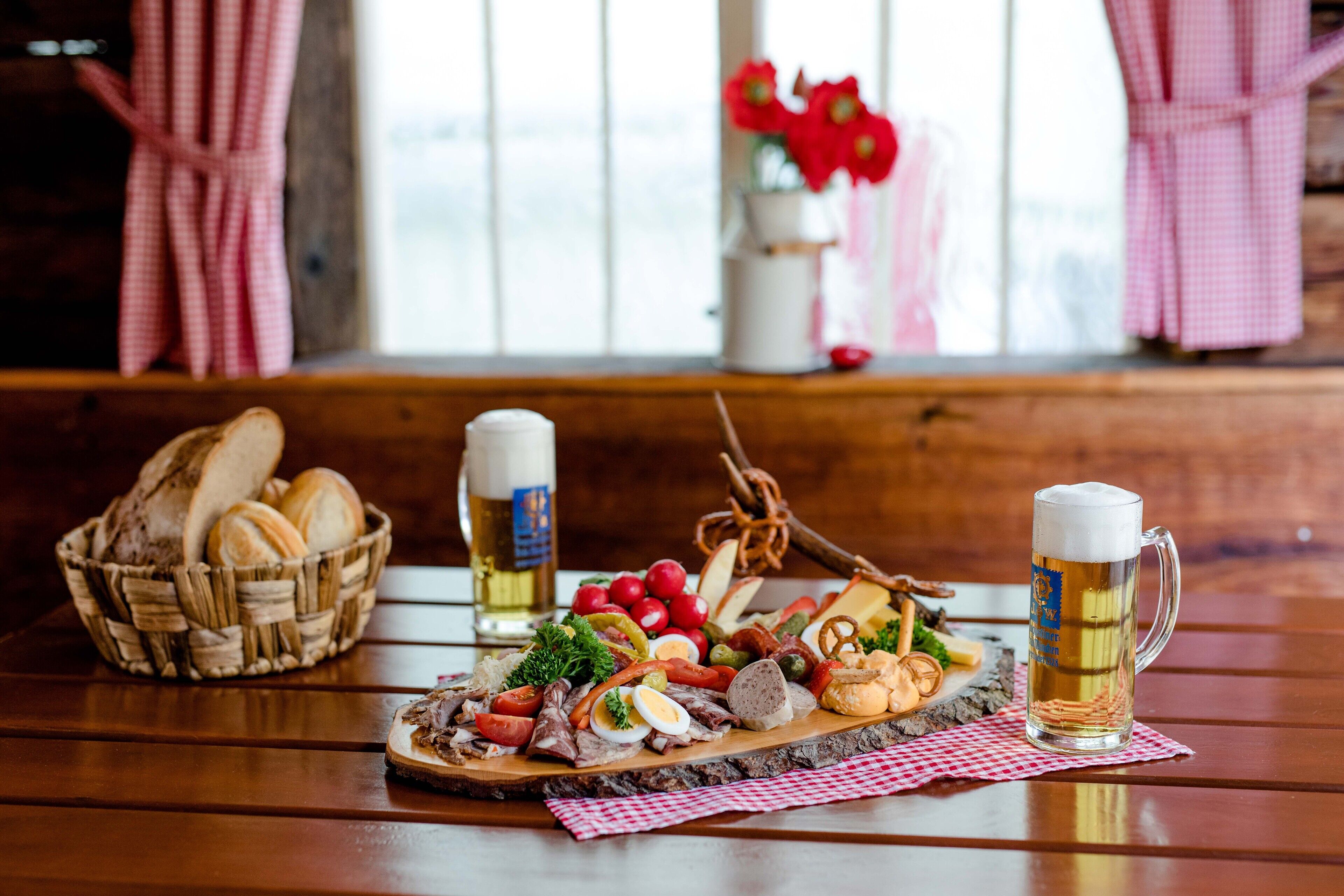 Una mesa de madera con una tabla de embutidos, dos jarras de cerveza y una cesta de pan.