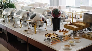 A buffet setup with various food items and serving equipment. - Gemma Hotel & Apartment Near Dragon Bridge  (Da Nang)