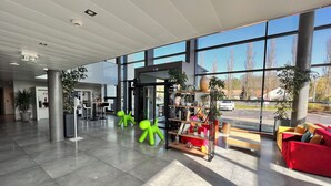 Un hall d’entrée spacieux au design moderne, comprenant un comptoir d’accueil, un espace salon et de grandes fenêtres offrant une vue sur l’extérieur.