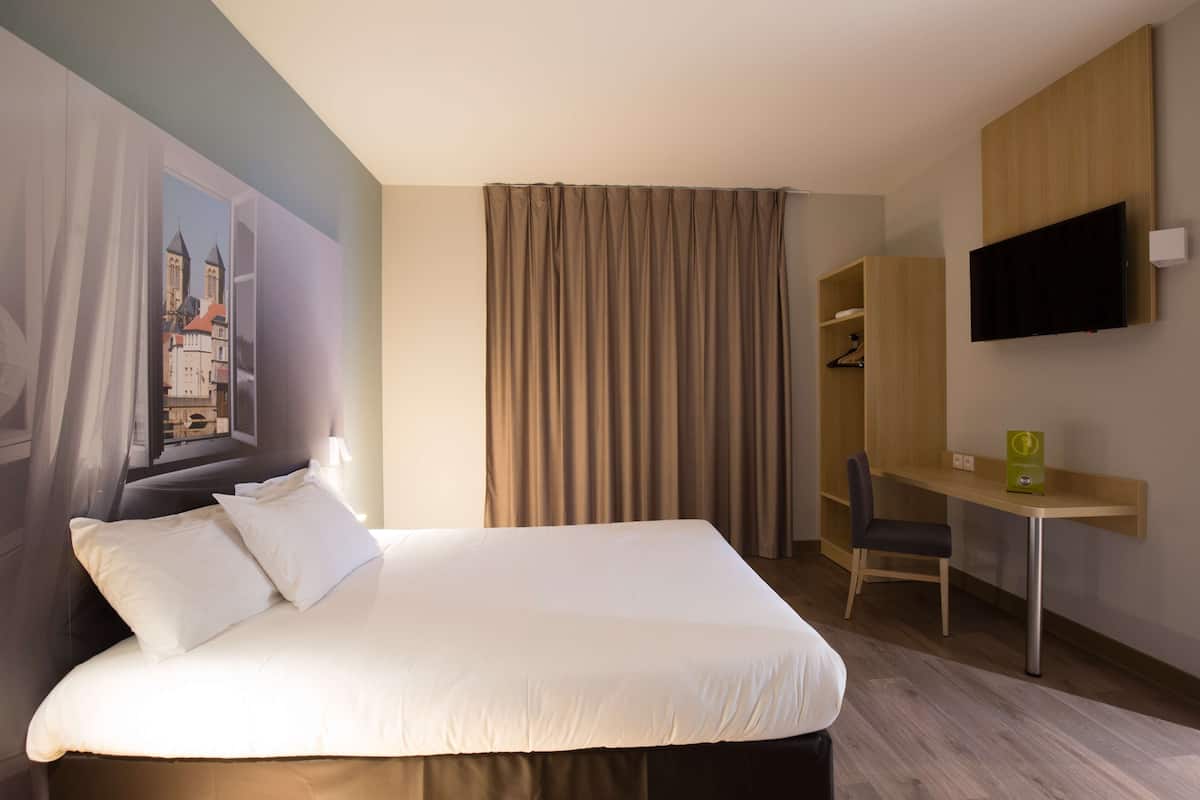 A hotel room with a bed, a desk, a chair, a TV, and a wardrobe.