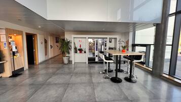 A spacious lobby with a reception desk, a vending machine, and a seating area with tables and chairs.