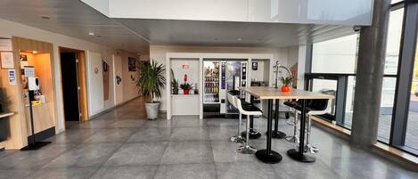 Un vestíbulo amplio con una mesa de recepción, una máquina expendedora y un área de descanso con mesas y sillas.