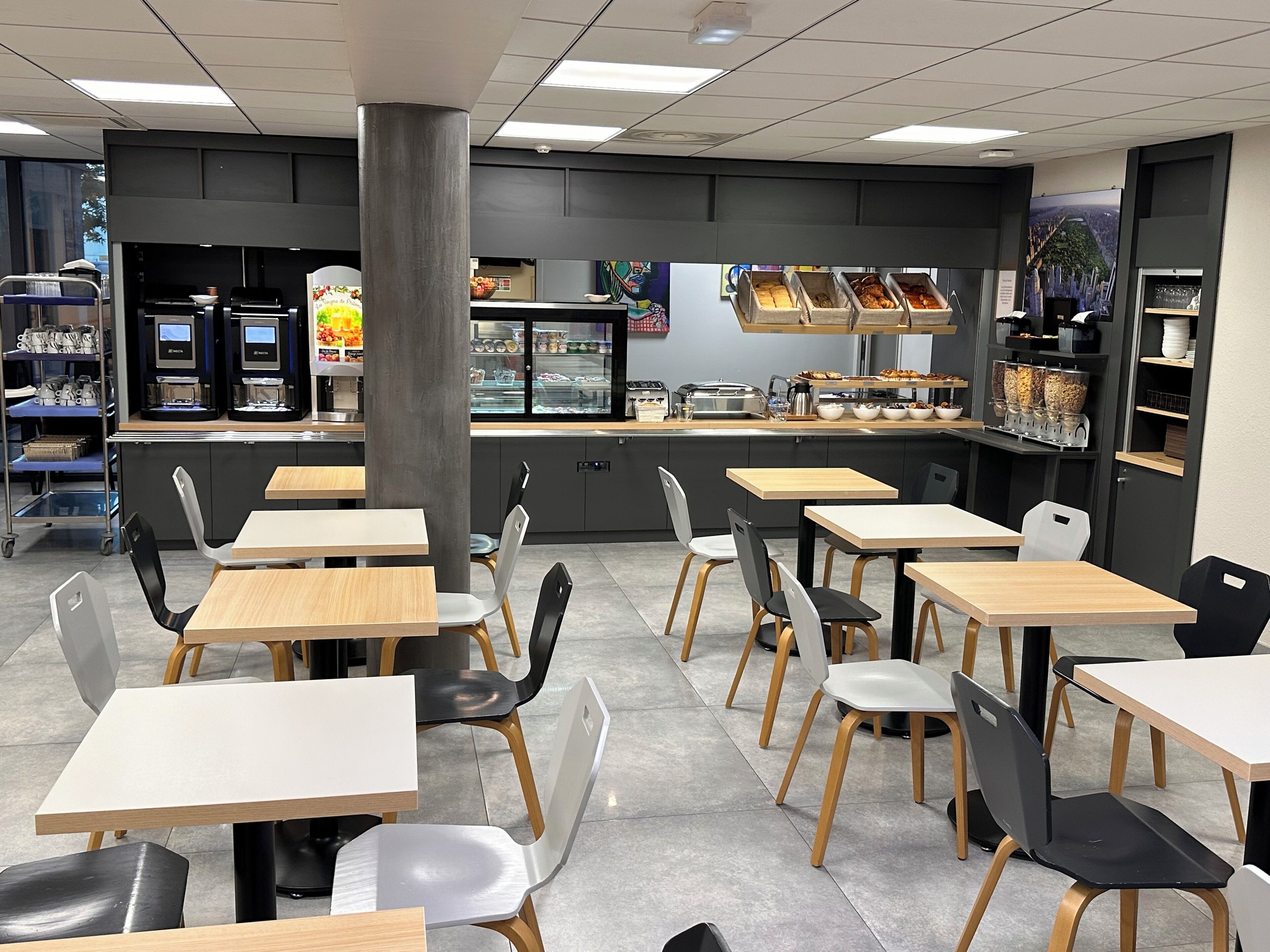 A modern cafe with multiple tables and chairs, a counter with food display, and a coffee machine.