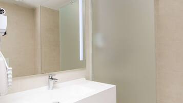 A modern bathroom with a large mirror, a white sink, and a glass shower enclosure.