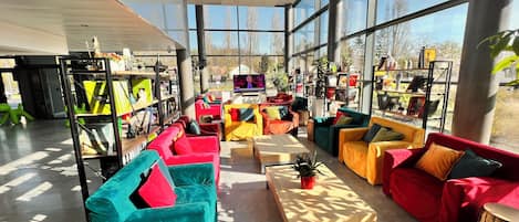 A spacious indoor area with large windows, multiple colorful sofas, and a variety of bookshelves filled with books and decorative items.