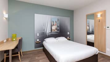 Ein Hotelzimmer mit Bett, Schreibtisch und Stuhl. Ein großes Fenster bietet Blick auf Gebäude.